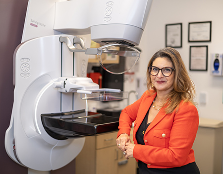 Woman in a red suit leaning her elbow on a mammography unit.